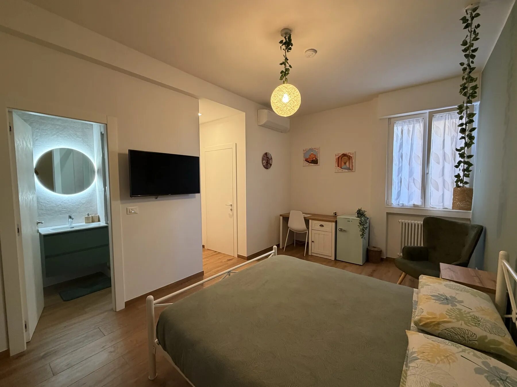 La camera, vista dall'ingresso: letto in ferro battuto e parete verde salvia