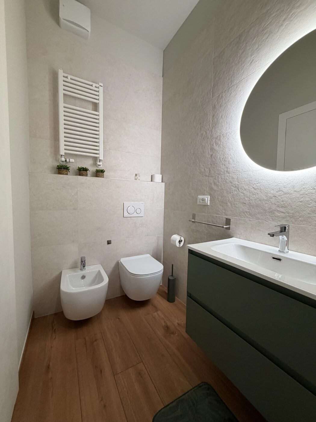 Il bagno privato: sanitari sospesi, bidet, scaldasalviette e mobile verde con specchio tondo retroilluminato