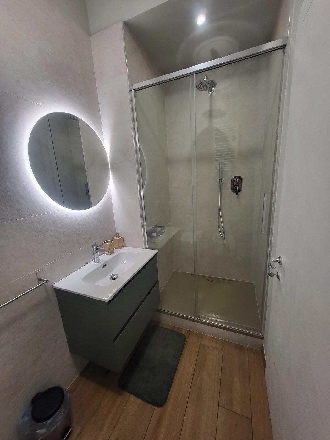 Il bagno privato: lavabo su mobile verde, specchio tondo retroilluminato e box doccia con soffione a pioggia