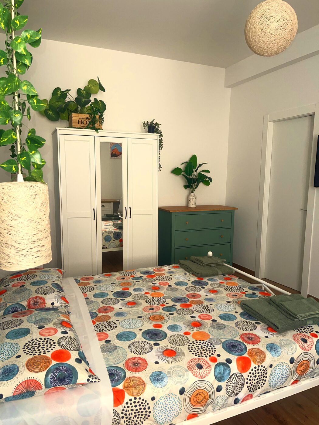 La camera dai piedi del letto: armadio a specchio, cassettiera verde con piano in legno e lampade in fibra intrecciata